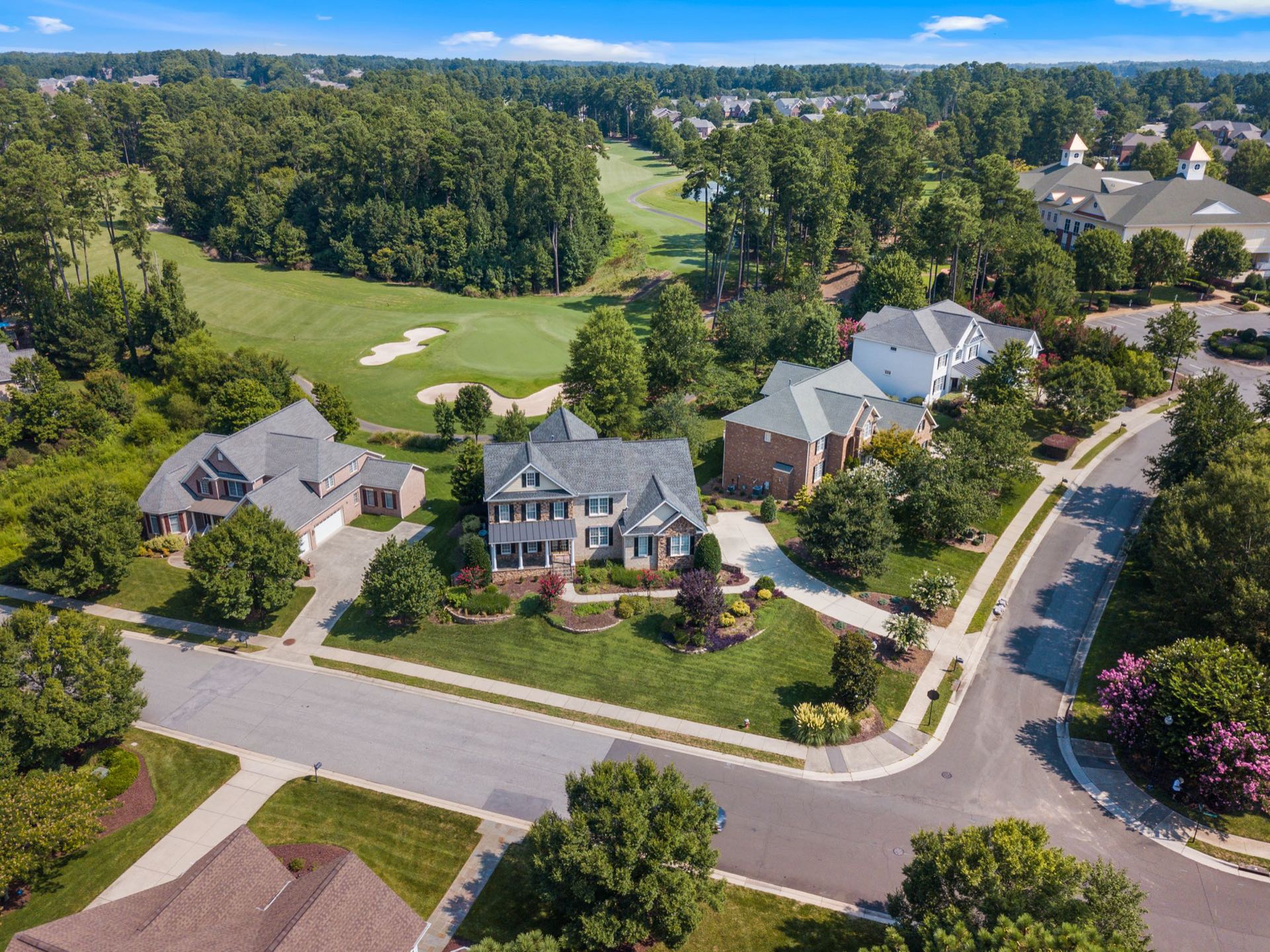Aerial view of an upscale tree-lined suburban neighborhood beside a golf course — the suburban lifestyle Ariella + Lukasz Realty Group serves